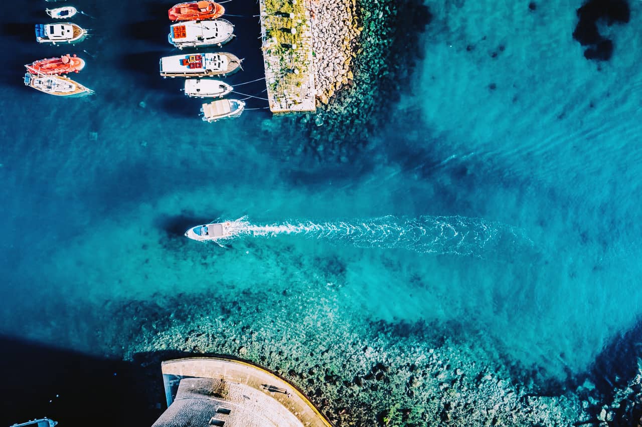 Vue de dessus : un petit bateau à moteur entre dans le port de Dubrovnik. L'eau est d'un bleu turquoise.